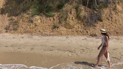 slow motion of attractive woman walking barefoot at the shore on sunny day in greece