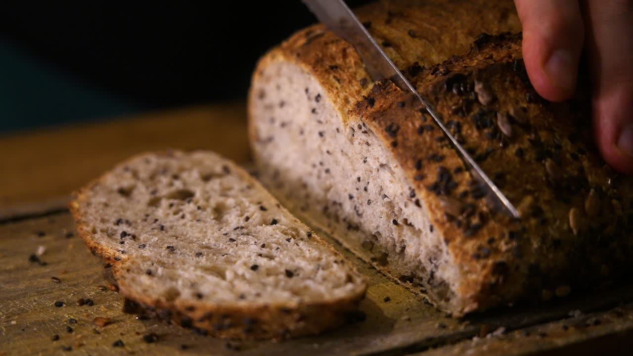Close-up of Hands Slicing Freshly Baked Seeded Bread on a Wooden Board