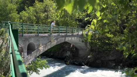 young man standing on a stone bridge and looking at flowing blue mountain rives