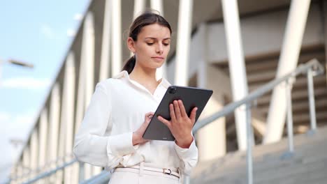 young businesswoman stands on stairs and works on an ipad medium shot