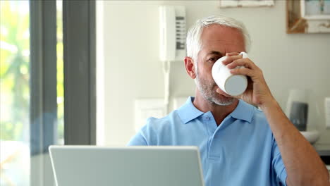 serious man using his laptop while drinking a coffee