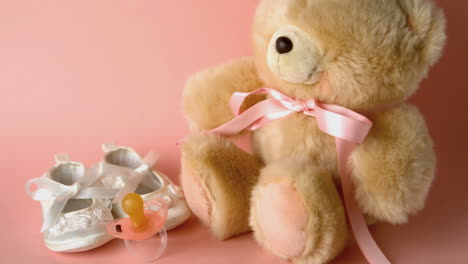 pink soother falling in front of baby shoes and a teddy bear