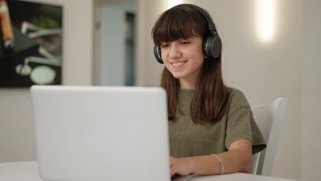 retrato de la chica adolescente linda en los auriculares sentada frente a la computadora portátil