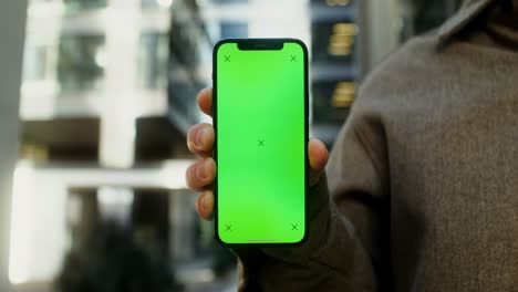 person holding a smartphone with a green screen