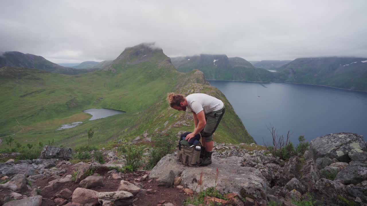 excursionista poniendo ropa en su mochila con las montañas segla al fondo en la isla senja, norte de noruega