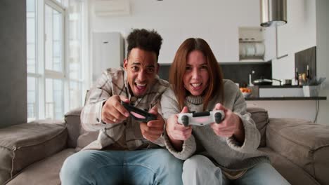 A-happy-Black-skinned-man-with-a-brunette-and-his-girlfriend-in-a-sweater-play-a-video-game-using-a-joystick.-Then-the-man-wins-and-the-girl-is-sad-about-her-defeat-in-a-modern-apartment-Sitting-on-the-sofa