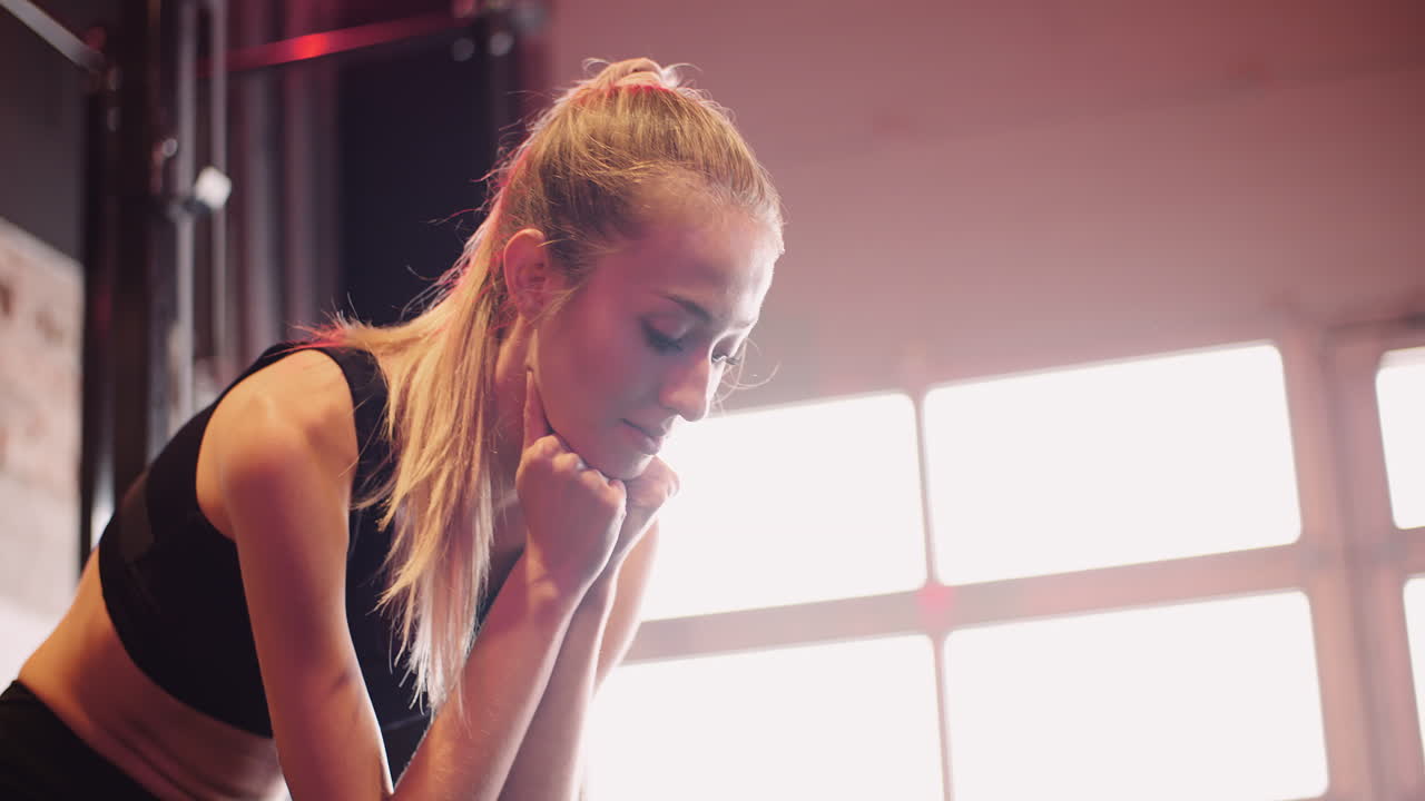 Rallentatore di una donna attraente e pensierosa in abbigliamento sportivo seduta in un club fitness.