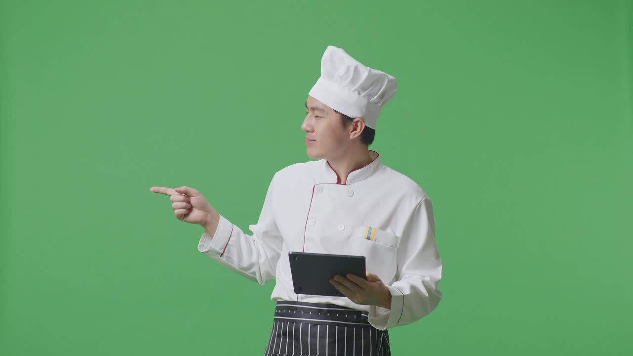 녹색 화면 배경 스튜디오 에 서 있는 동안 태블릿 을 사용 하고  을 가리키는 아시아 사람 요리사
