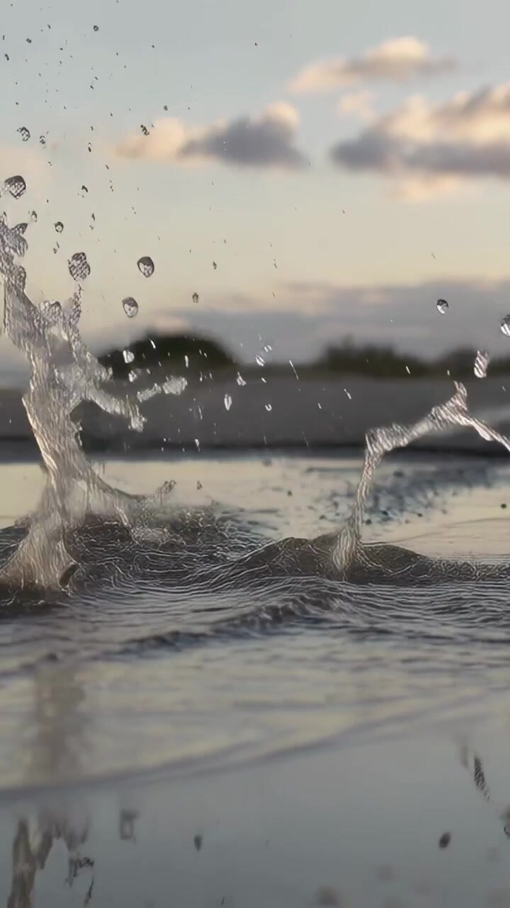 Vertical video: Rolling wheel splashing puddle on tarmac while driving at sunset, rim reflection