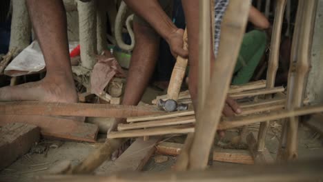 Unrecognized-poor-labour-hammering-nails-on-bamboo-stick
