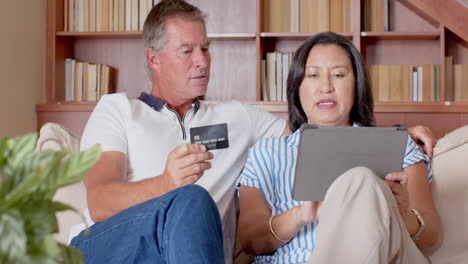 senior diverse couple shopping online using tablet and credit card at home