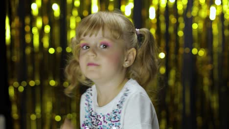 stylish child dancing fooling around, make faces. girl posing on background with foil golden curtain