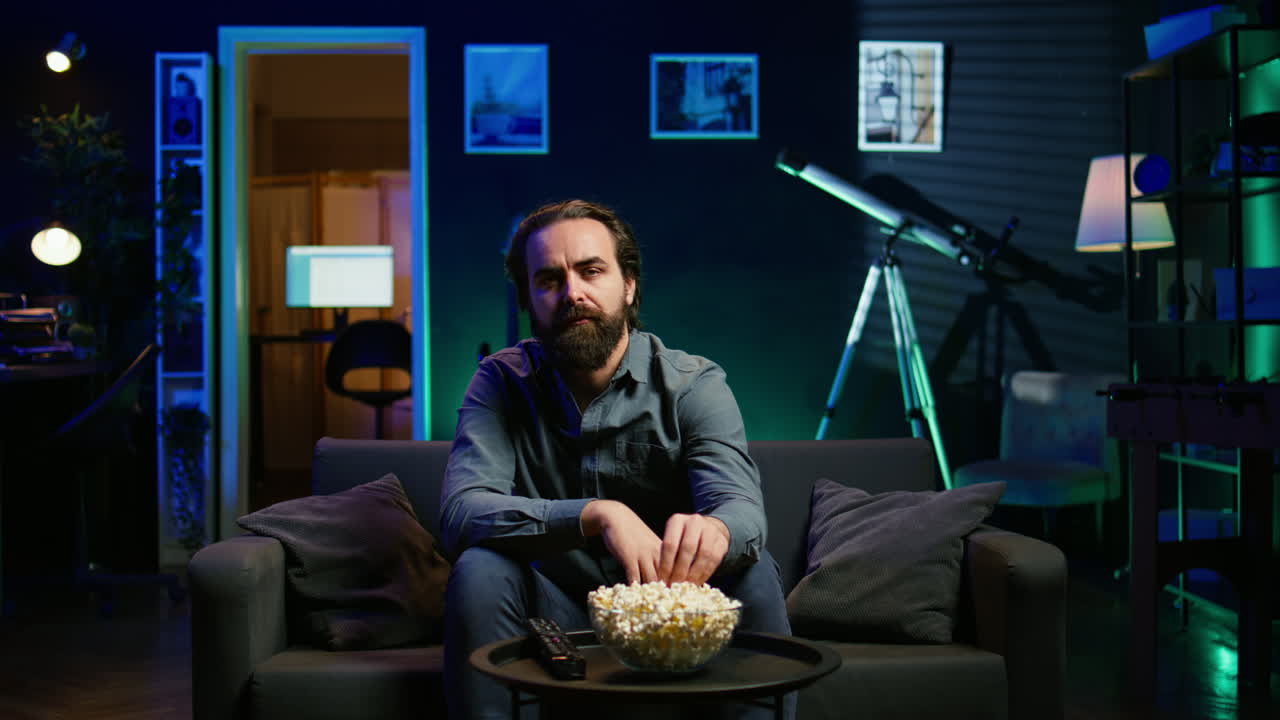 hombre disfrutando de un plato de palomitas de maíz y sonriendo mientras ve programas de cable en la televisión