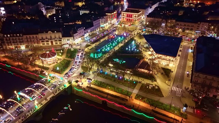 Ripresa aerea da drone in movimento dalla Mayenne verso Piazza 11 Novembre a Laval, che mostra decorazioni natalizie luminose, animali luminosi, la giostra, il mercato coperto e il ponte Aristide Briand decorato
