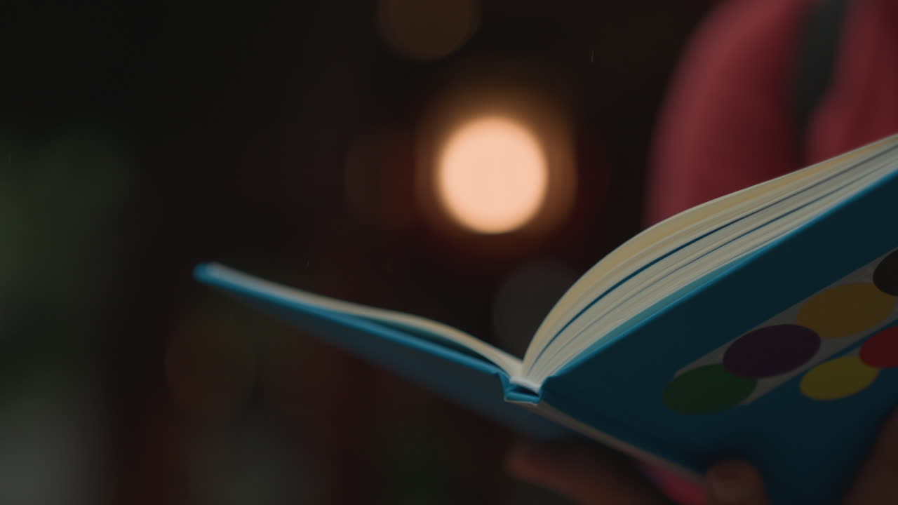 Mani che tengono un quaderno colorato di notte, morbida luce bokeh incornicia le pagine aperte e il caldo bagliore di una lampada, una persona sfoglia lentamente le pagine, atmosfera intima e accogliente che suggerisce di scrivere un diario prima di dormire, tranquilla riflessione