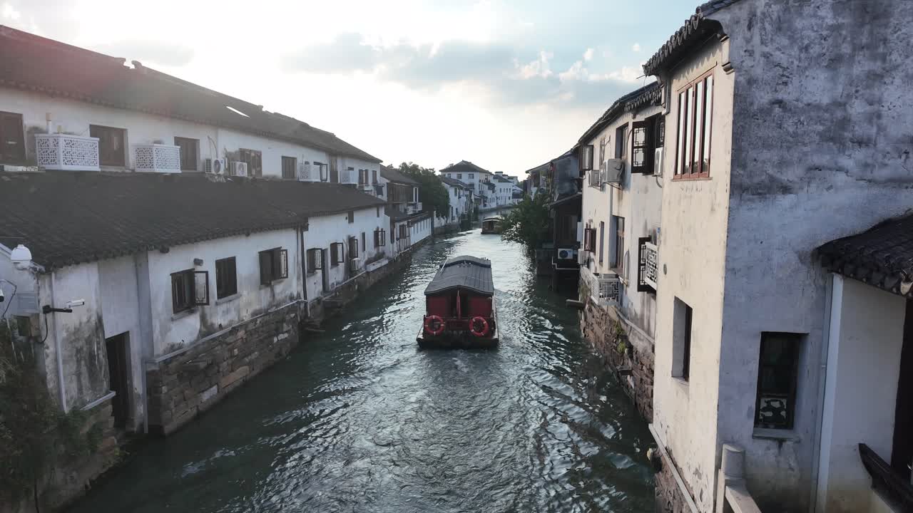 Traditional Chinese boat gliding through historic Hangzhou canal, flanked by whitewashed buildings with tiled roofs, capturing the tranquil charm of ancient waterways at golden hour
