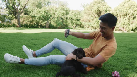 asian man enjoying sunny day in park, playing with happy puppy