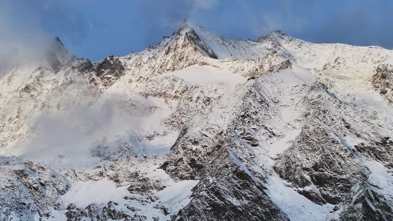 Mount Dom Ulrichschorn Gumshoe Stalden Saas Fee ski resort Saastal Swiss Alps Valley Switzerland drone aerial morning sunrise snow mountain peaks low clouds fog layer slow pan left motion