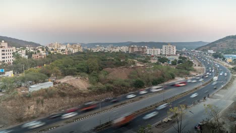 busy traffic time lapse of day time on national highway, cityscape view, residential buildings and mountains, maharashtra, india