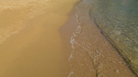 Small-waves-and-sea-foam-wash-gently-over-sand,-natural,-tropical-beach