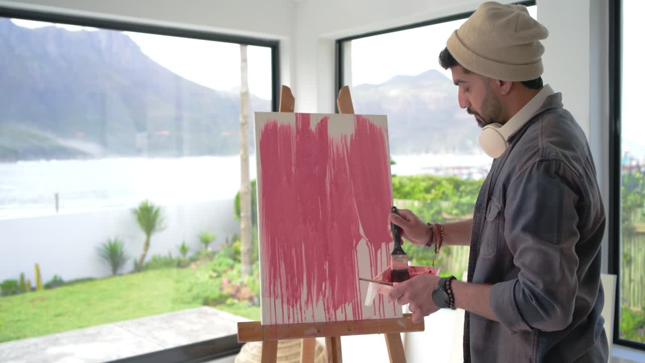 After selecting brush, artist is dipping into pink paint and filling canvas near window