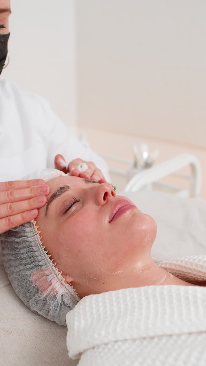 Cosmetologista massageia suavemente o rosto da mulher com limpeza de espuma durante o procedimento de cuidados com a pele em uma clínica de spa