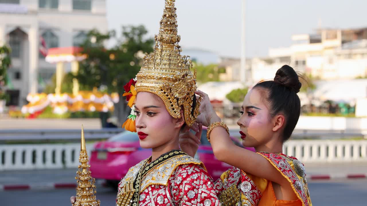 Un assistente sistema un tradizionale copricapo dorato su un ballerino Khon thailandese all'aperto a Bangkok.