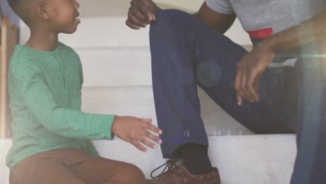 animation of lights over midsection of happy african american son tying fathers shoe