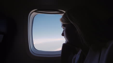 silueta de una mujer joven volando en un avión mirando por la ventana