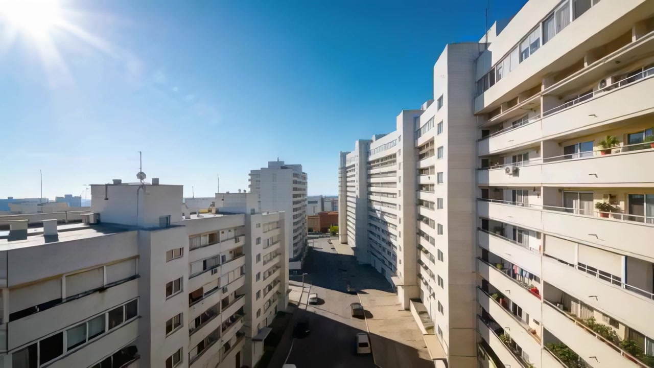 Movendo a câmera para frente, revelando a vista de uma rua residencial com apartamentos brancos, carros e roupas estendidas.