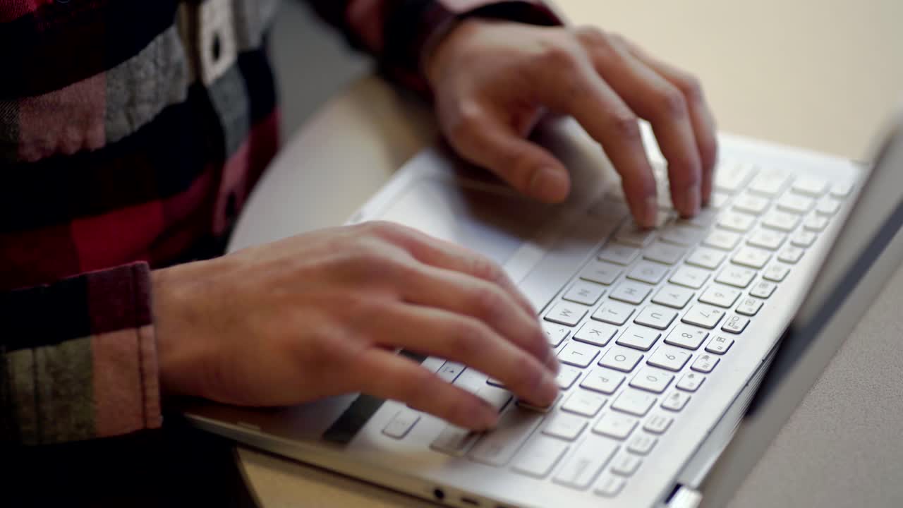 un uomo che indossa una camicia di flanella rossa e nera che digita sulla tastiera del suo laptop - primo piano pan a destra