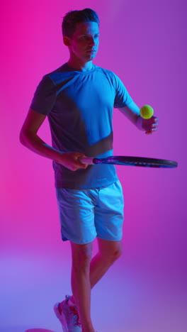 Vertical-Video-Studio-Shot-Of-Male-Tennis-Player-Bouncing-Ball-On-Racket-Against-Low-Key-Colourful-Mixed-Lighting