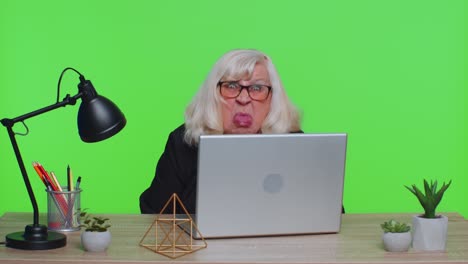 una mujer de negocios mayor madura se esconde detrás de una computadora portátil, haciendo una cara graciosa, haciendo tonterías.