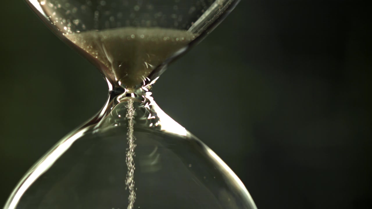 Close-up of Sand Flowing Through an Hourglass on a Dark Background