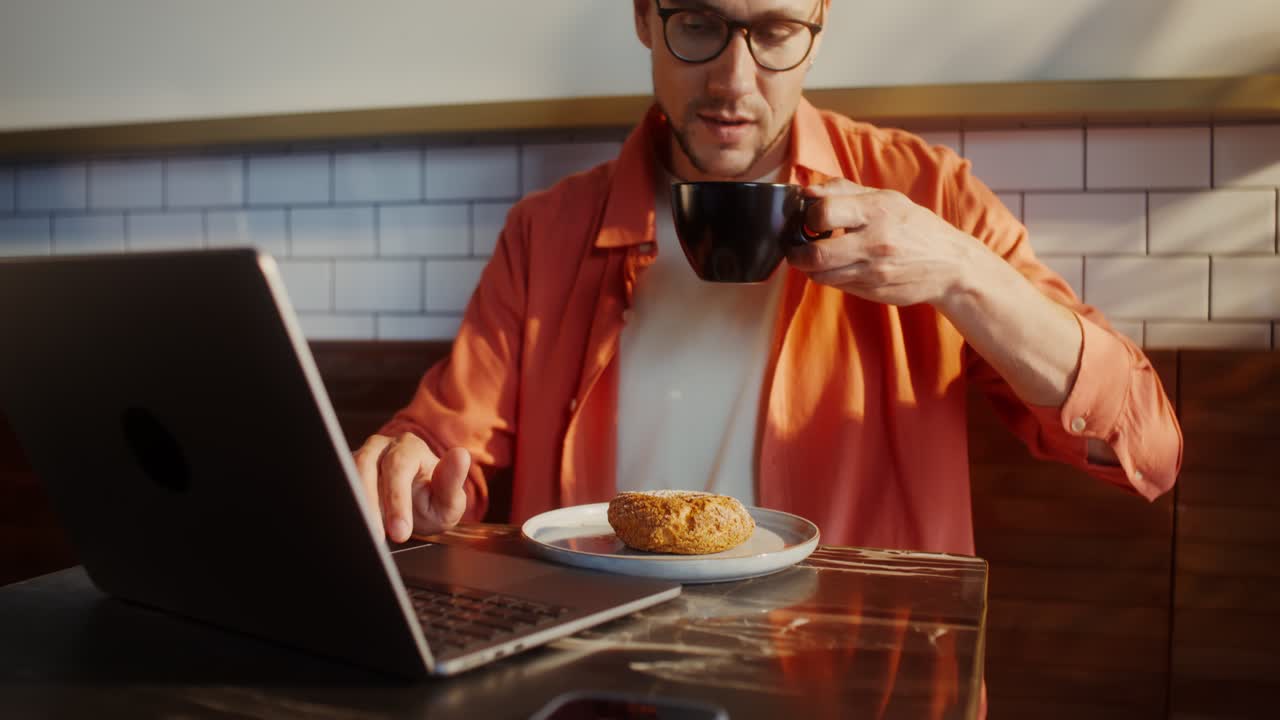 hombre trabajando en una computadora portátil en un café con café y pastel