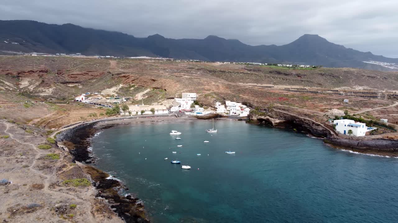 Drone view of a small natural port with fishing boats and with mountains in the background in Puertito de Adeje, Tenerife, Canary Islands, Spain.