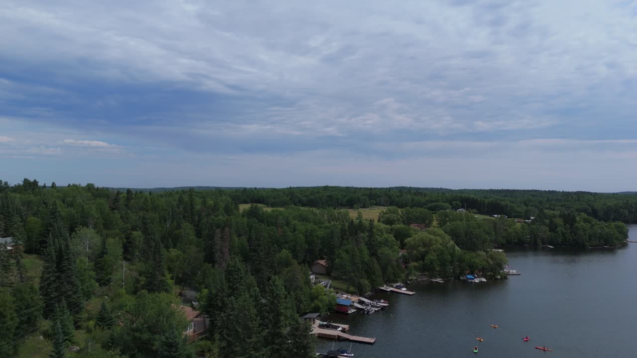 Aerial drone footage of a calm lake with boats, shoreline docks, and dense forest under a dramatic cloudy sky