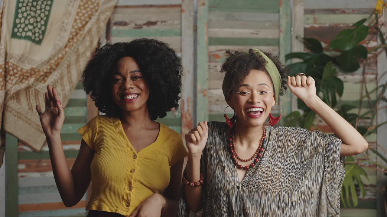 Two stylish african american ladies wearing traditional clothes dancing together, enjoying dynamic music, slow motion