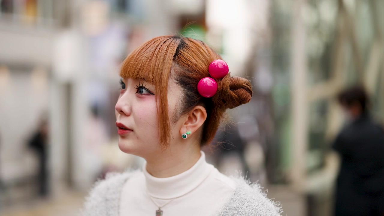 東京の原宿通りで振り返る、ジンジャー色のスペースバンズヘアとピンクのアクセサリーを身につけた若いアジア人女性