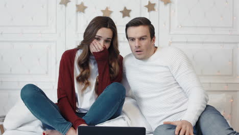 una pareja molesta viendo noticias horribles en la computadora en casa juntos.