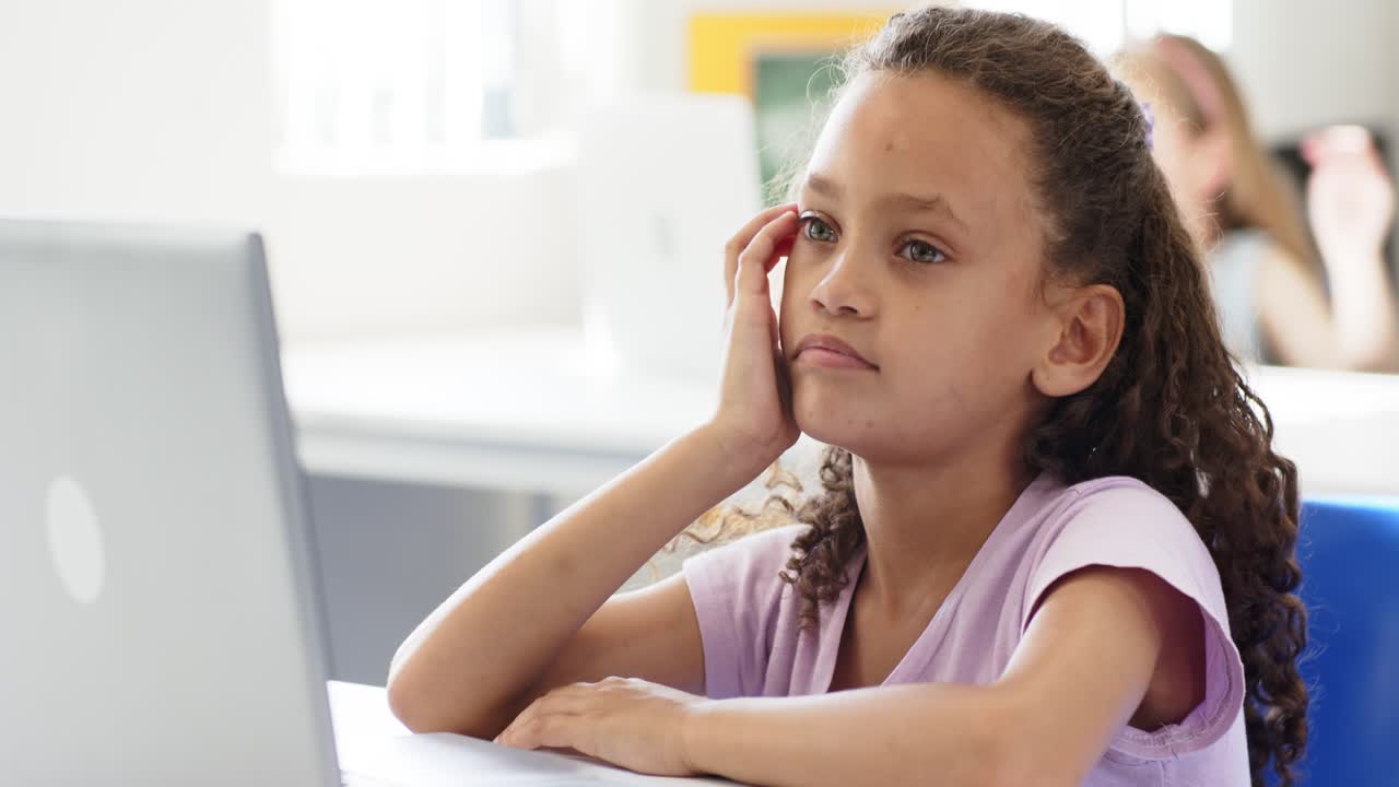 Giovane studentessa nota un compagno di classe sfocato, sposta lo sguardo e si strofina l'orecchio alla scrivania con un laptop.