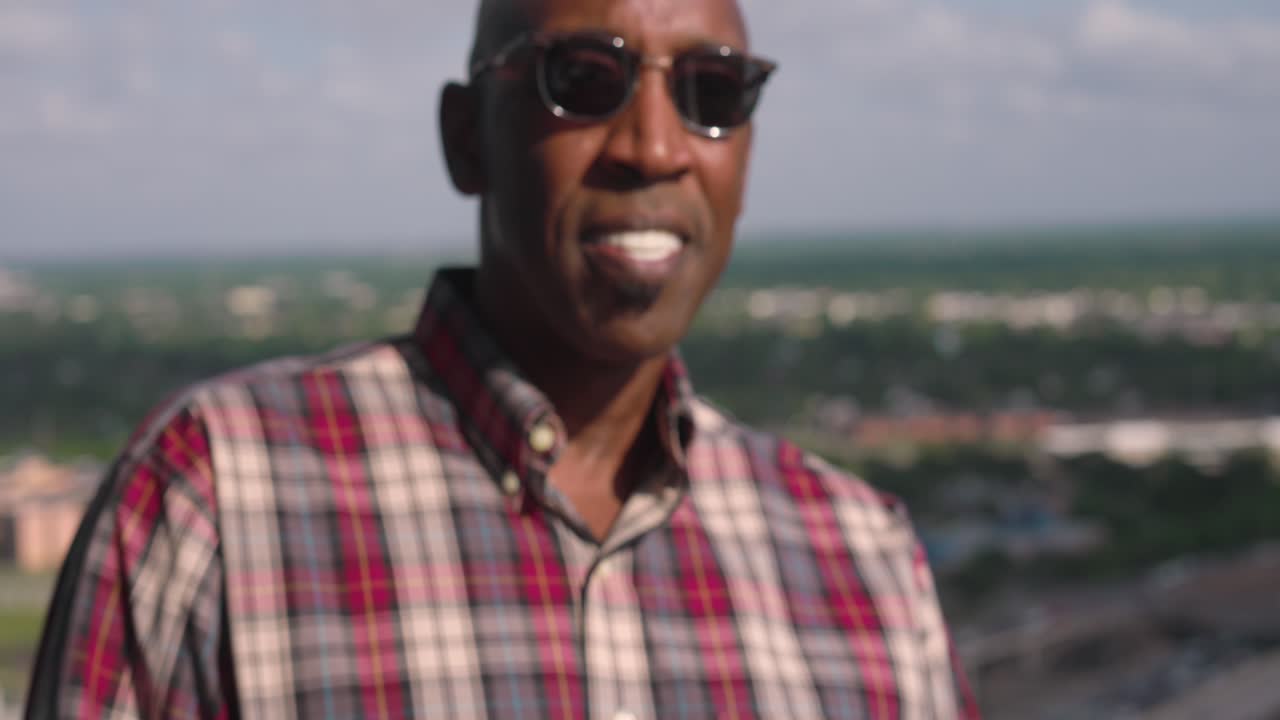 hombre negro con gafas de sol sonriendo de pie en el balcón