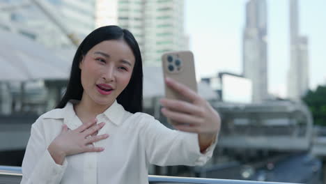 young asian woman takes a selfie or makes a video call in the city