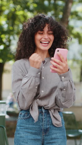 Caucasian-woman-use-mobile-smartphone-celebrating-win-good-message-news-outdoors-on-city-street