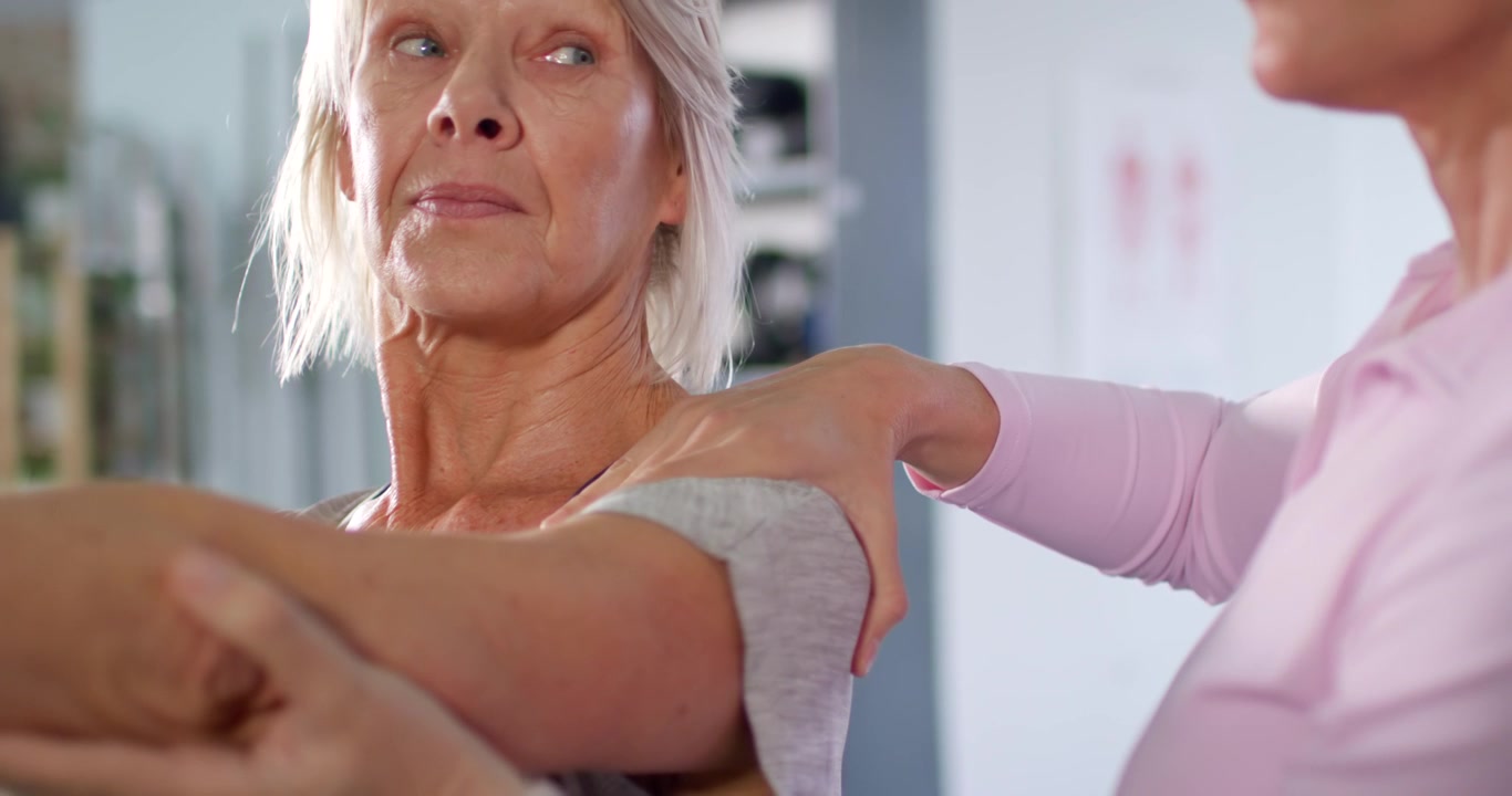 Senior female patient extending right arm at rehab clinic after clinician hand placement and cues