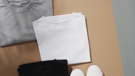 video of flat lay of multi coloured t shirts with copy space on brown and grey background