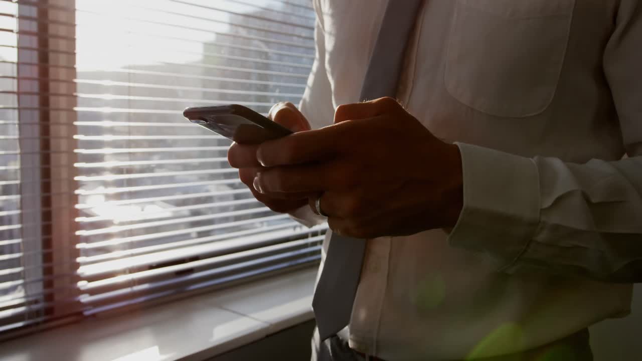 Mid section of young Caucasian male executive using mobile phone near window in modern office 4k