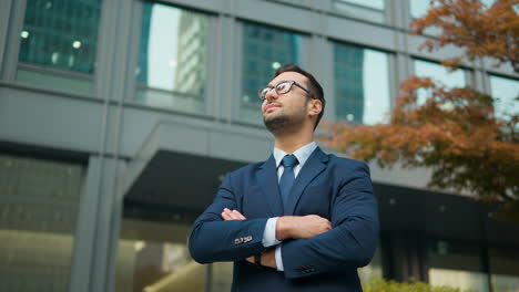 confident business man standing in front of office building, arms crossed looking up with admiration