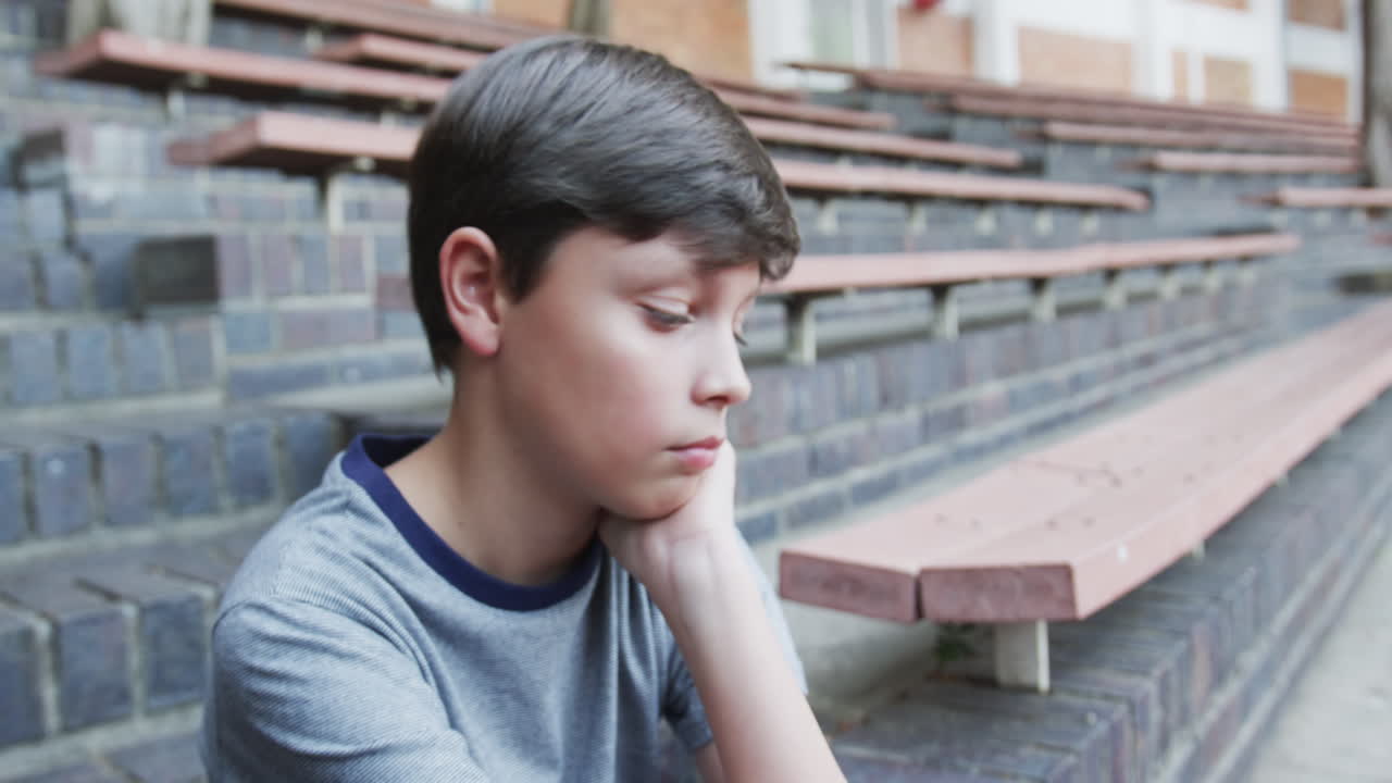 Sitting on bleachers, boy wiping face with hand at school
