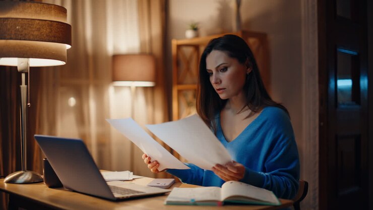Stressed remote worker reading documents at dark home closeup. Worried woman